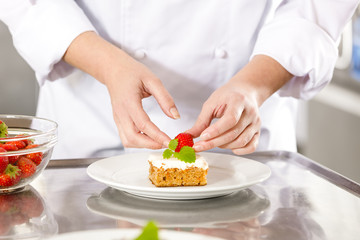Obraz na płótnie Canvas Close-up of chef decorating dessert cake with strawberry