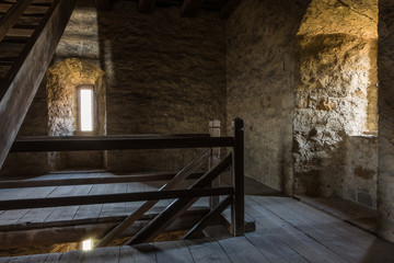 Fototapeta na wymiar Dark room with stone walls window and wooden staircase