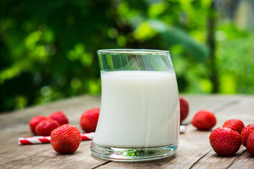 Glass of milk and ripe strawberry on the rustic wooden table