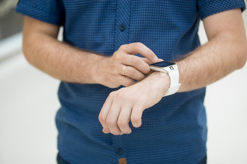 Close-up of torso of young man touching display on his smart watch, using internet, messaging, making call, or using app
