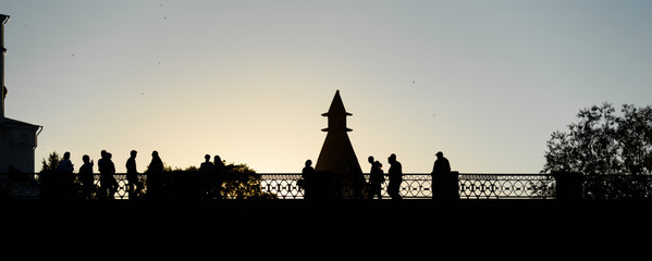 Silhouettes of people walking across bridge against the sky