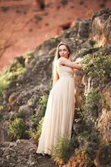 Fototapeta na wymiar Attractive young woman in long dress standing on the rocks