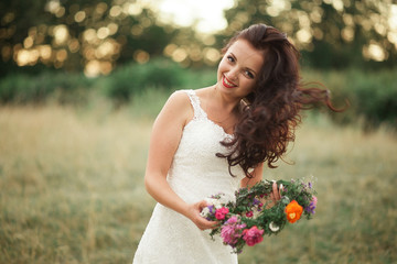 Bride. Beautiful young blond woman in the park with flower wreath and bouquet on a warm summer day