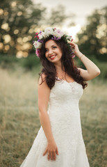 Fototapeta na wymiar Bride. Beautiful young blond woman in the park with flower wreath and bouquet on a warm summer day