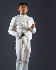 Fencing athlete posing with a sword or epee on gray background
