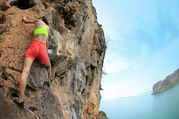 young woman rock climber climbing at seaside mountain cliff