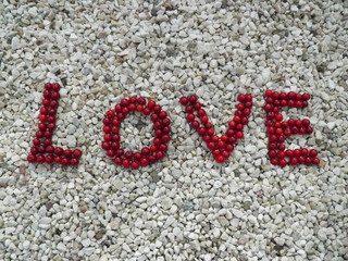 Słowo "Love" z czerwonych wiśni na białych kamykach