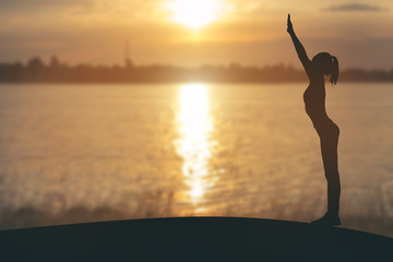 silhouette of woman practicing yoga on the river at sunset