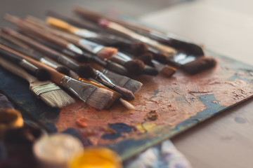 Different size paintbrush collection on an old palette with oil paint colors blend and a gouache set