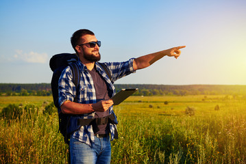 Healthy adult in sunglasses with rucksack holding a tablet and p