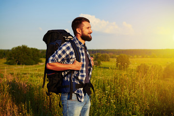 Side view of man with rucksack standing in the field and smiling