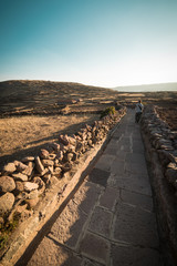 Tourist walking on the Inca Trail at sunset, Amantani' Island, Titicaca Lake, scenic travel destination in Peru. Travel adventures and vacations in the Americas. Toned image, vintage style.