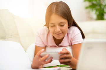 Happy girl using a mobile phone lying on the bed at home