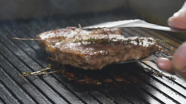 A cook turns up a steak of meat on a grill in slow motion