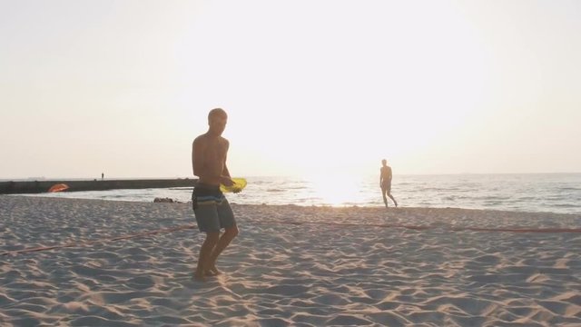 Two guys playing frisbee on the beach during sunrise, slow motion