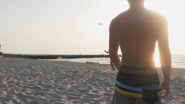 Two guys playing frisbee on the beach during sunrise, slow motion