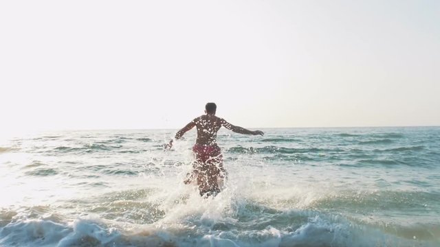 Two friends running and jumping in the sea during sunset, slow motion