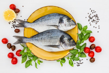 Fresh dorado fish on yellow plate on white wooden table. Top view, copy space.