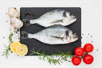 Fresh dorado fish on slate cutting board, rosemary, garlic, lemon and tomatoes. Top view, copy space.