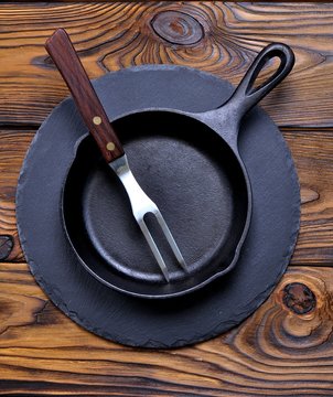 Iron frying pan on a serving board on wooden background.