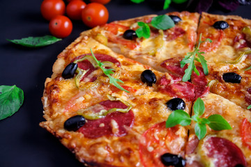 Homemade pizza with salami, black olives and basil.