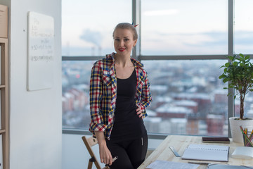 Obraz premium Young woman wearing casual bright shirt standing in light spacious office, her workplace, ready for work day, smiling, looking at camera.