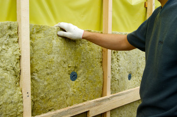 The man is engaged in construction work on the exterior isulation of the house with mineral wool
