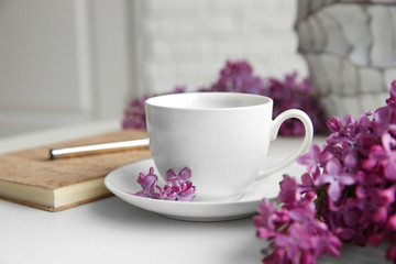 Purple lilac flowers and cup on white table