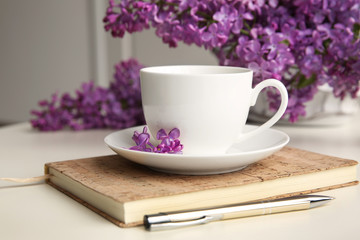 Purple lilac flowers and cup on white table