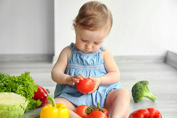 Cute baby girl with vegetables on wooden floor