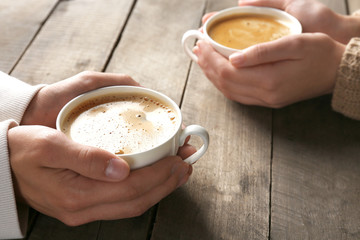 Lovely couple holding cup of coffee in hands on wooden background
