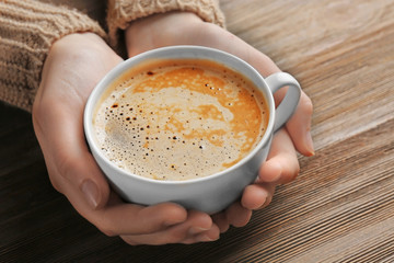 Female hands holding cup of coffee on wooden background