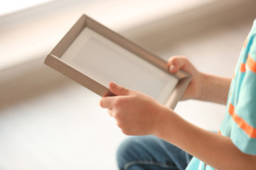Child's hands holding photo frame on light background
