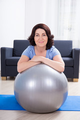 slim sporty mature woman doing exercises with fitness ball at ho