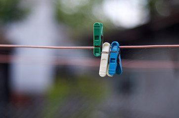 Green, white, blue clothes peg on a washing line/Closeup of Colorful clothes peg on a rope isolated on light blurred background 

