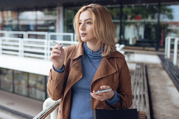 Outdoor portrait of pretty blonde young girl smoking a cigarette.