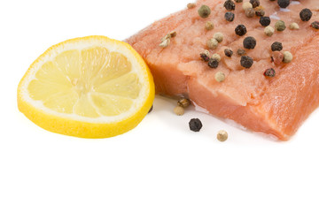 Frisches Lachslfilet, mit Pfefferkörner und einer Zitronescheibe dekoriert. Auf weißem Hintergrund.