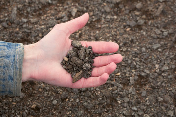 Hand of the farmer holding handful of infertile earth