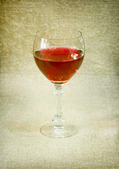 One glass with red wine against brown drapery
