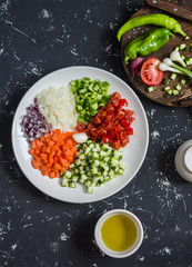 Fresh chopped vegetables - tomatoes, zucchini, carrots, tomatoes, onions, peppers on a dark background. Ingredients for ratatouille. Top view
