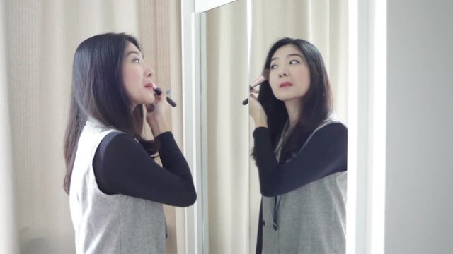 Asian portrait beautiful woman making or applying make-up with brush on face and looking in the mirror in full HD