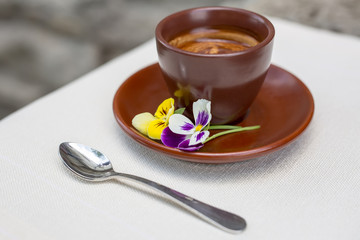 Brown Cup of espresso is decorated with yellow and purple violets