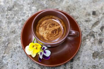 Brown Cup of espresso is decorated with yellow and purple violets