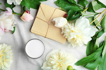 Fototapeta na wymiar Composition with beautiful peony flowers and envelopes on white fabric, top view