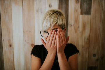 Young girl in glasses covering face with hands