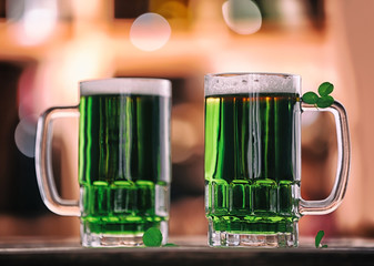 Glasses of green beer with clover leaves on blurred bar background