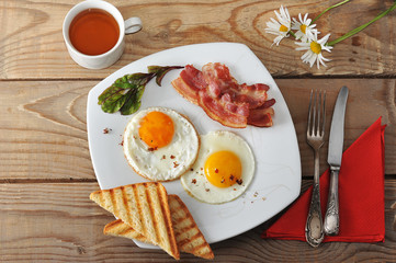 Breakfast - fried eggs, toast, bacon and tea and chamomile on wo