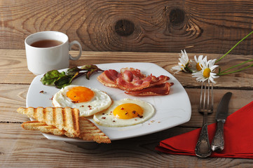 Breakfast - fried eggs, toast, bacon and tea on wooden backgroun