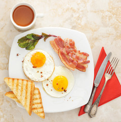 Breakfast - fried eggs, toast, bacon and tea on marble backgroun