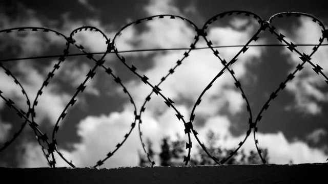 Barbed wire at the top of fence against the gloomy, dark evening sky with clouds.Black and white color correction